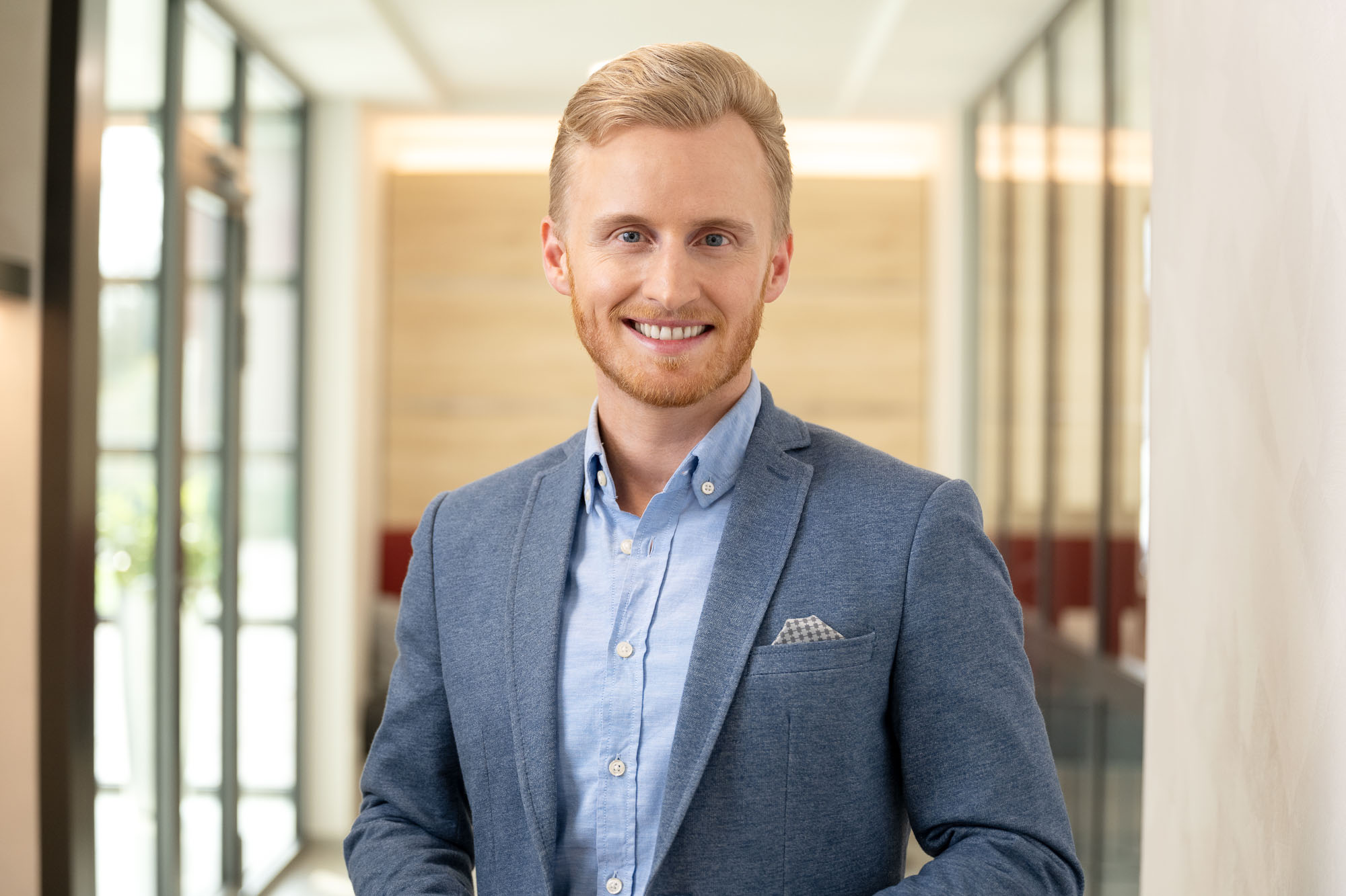 Junger Mann im blauen Blazer mit Einstecktuch und hellblauem Hemd in einem Flur