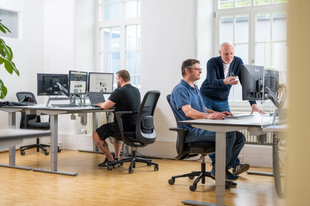 Drei Personen im Büro von e3 in der Rommelmühle, eine Absprache am Schreibtisch