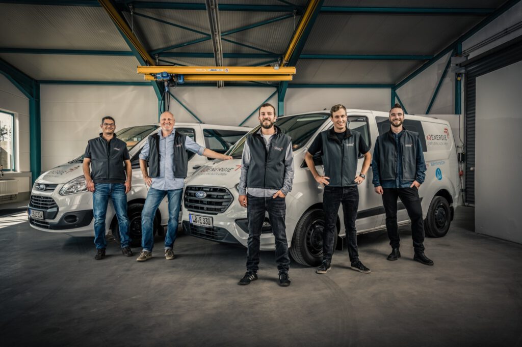 Fünf Personen von e3 vor zwei Servicefahrzeugen in der Halle