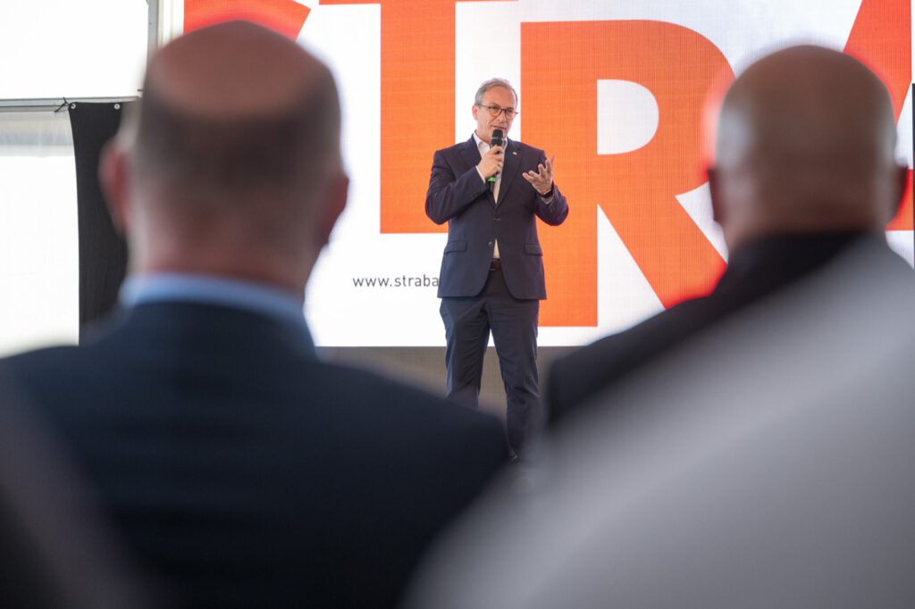 Bürgermeister Reiner Breuer spricht mit Handmikrofon vor dem großen STRABAG-Schriftzug