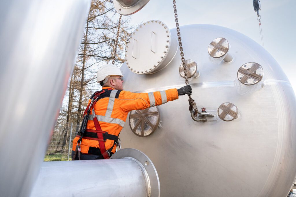 Monteur hängt die Kranketten am Deckel eines liegenden Edelstahltanks ein