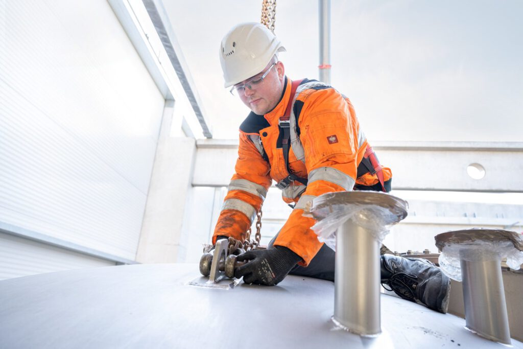 Monteur mit Auffanggurt arbeitet oben auf einem Edelstahltank in der Halle