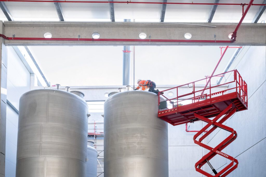 Aufgestellte Edelstahltanks in der neuen Halle, daneben eine rote Hubarbeitsbühne