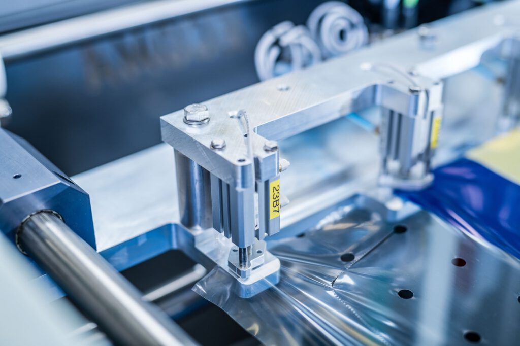 Greifer der Verpackungsanlage zieht Folie über eine Kiste, ECOMA Maschinen, Weyhe-Dreye