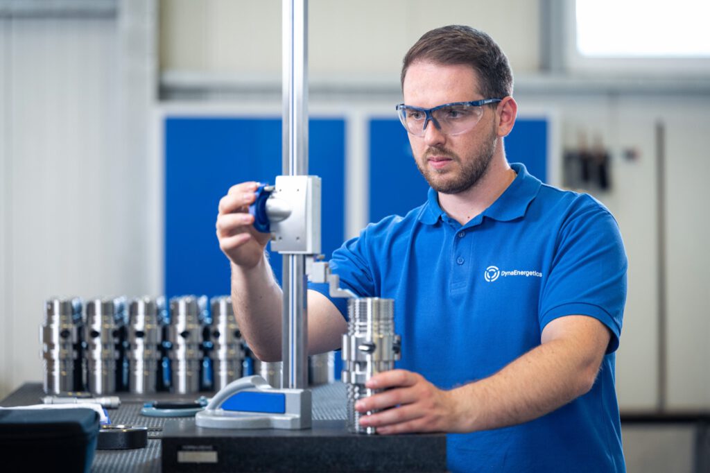 Mitarbeiter von DynaEnergetics mit Schutzbrille prüft ein Bauteil am Messgerät