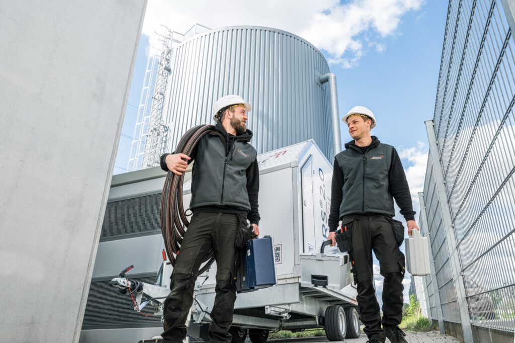 Zwei Personen mit Helm und Werkzeugkoffern verlassen den Anhänger an einem Heizwerk