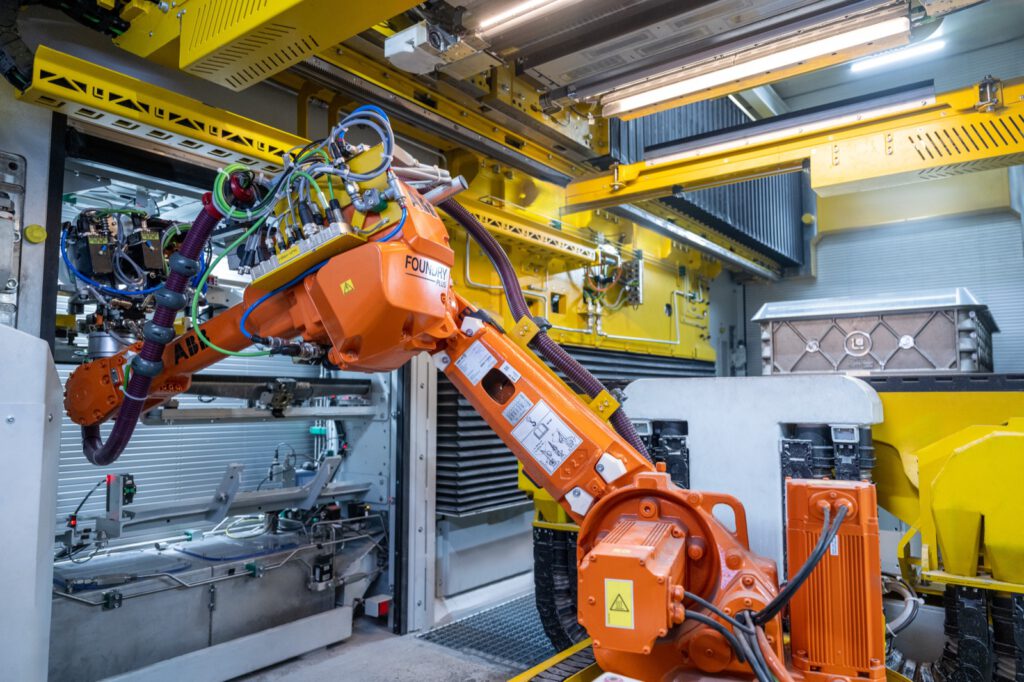 Orangefarbener Roboter mit vielen Leitungen in der Anlage, im Hintergrund gelbe Portale