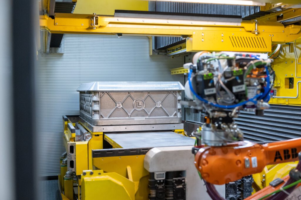 Orangefarbener Roboter mit Greifer vor einer gelb eingefassten Box in der 3D-Drucklinie