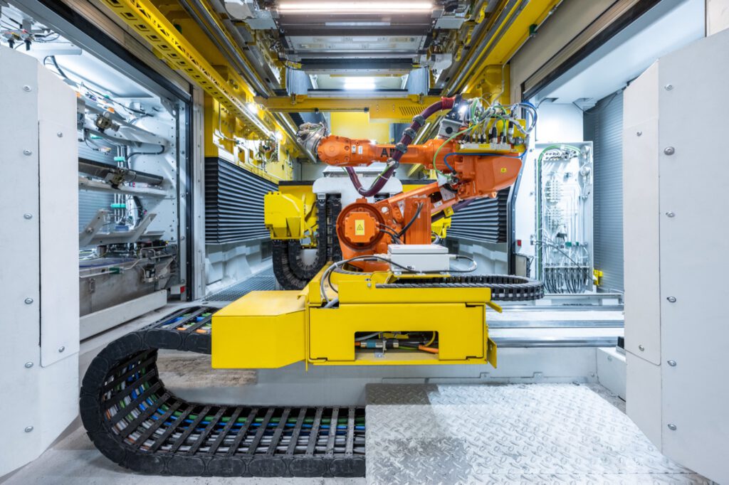 Blick in die 3D-Drucklinie: orangefarbener Roboter über gelber Technik, davor eine Energiekette