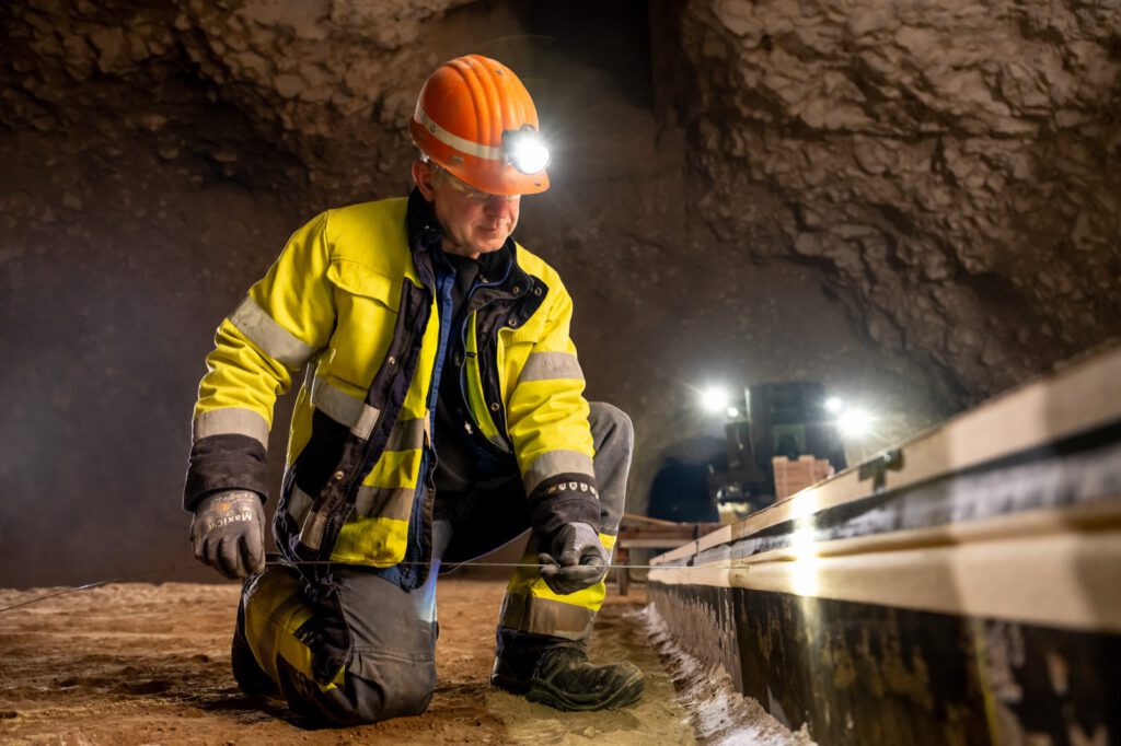 Mitarbeiter mit Helm und Stirnlampe kniet in der Grube neben einer vorbereiteten Platte