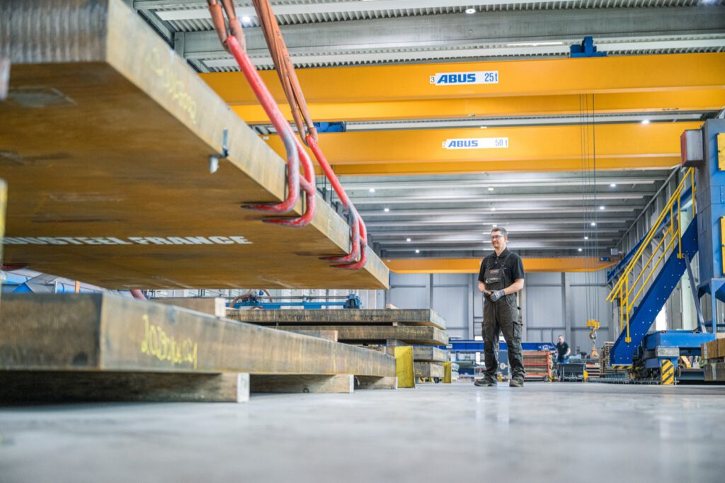 Eine schwere Platte hängt am Hallenkran, darunter ein Mitarbeiter in der Halle