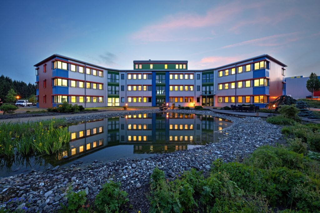 Verwaltungsgebäude von NobelClad in Liebenscheid zur blauen Stunde, beleuchtete Fenster spiegeln sich im Teich