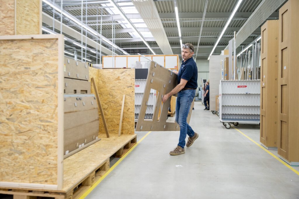 Mitarbeiter trägt ein großes Bauteil durch die Produktionshalle von Oldenburger Interior in Dinklage