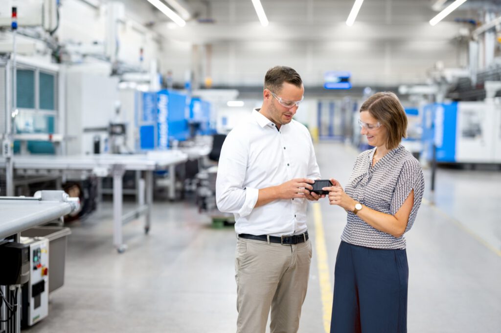 Mitarbeiter und Mitarbeiterin von K-TECH besprechen in der Fertigungshalle ein Bauteil