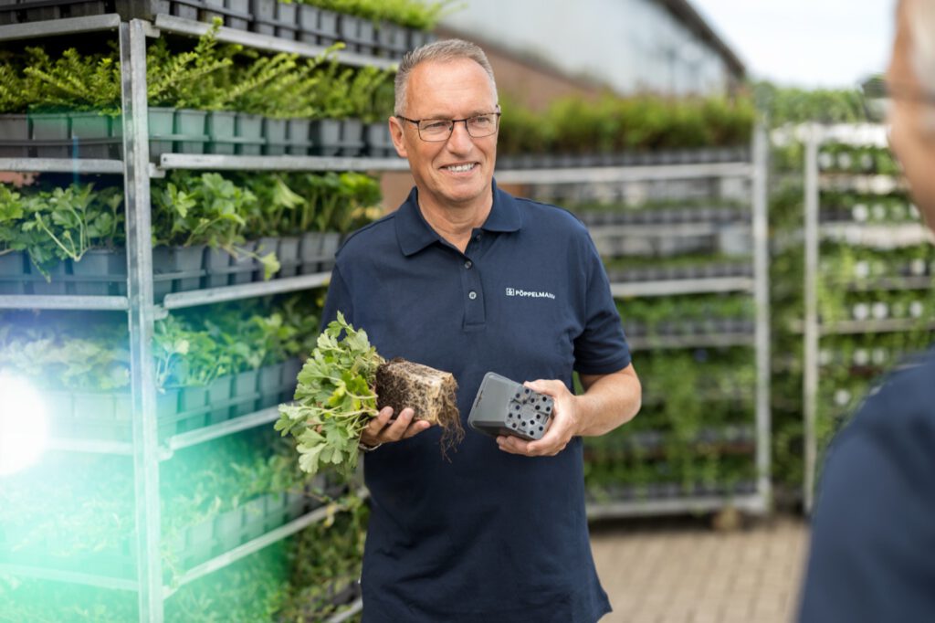 Mitarbeiter von TEKU zeigt in einer Gärtnerei eine Jungpflanze mit Wurzelballen und einen Topf