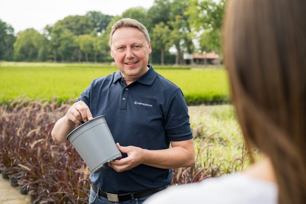 Mitarbeiter von TEKU hält draußen vor einem Feld einen grauen Pflanztopf in den Händen