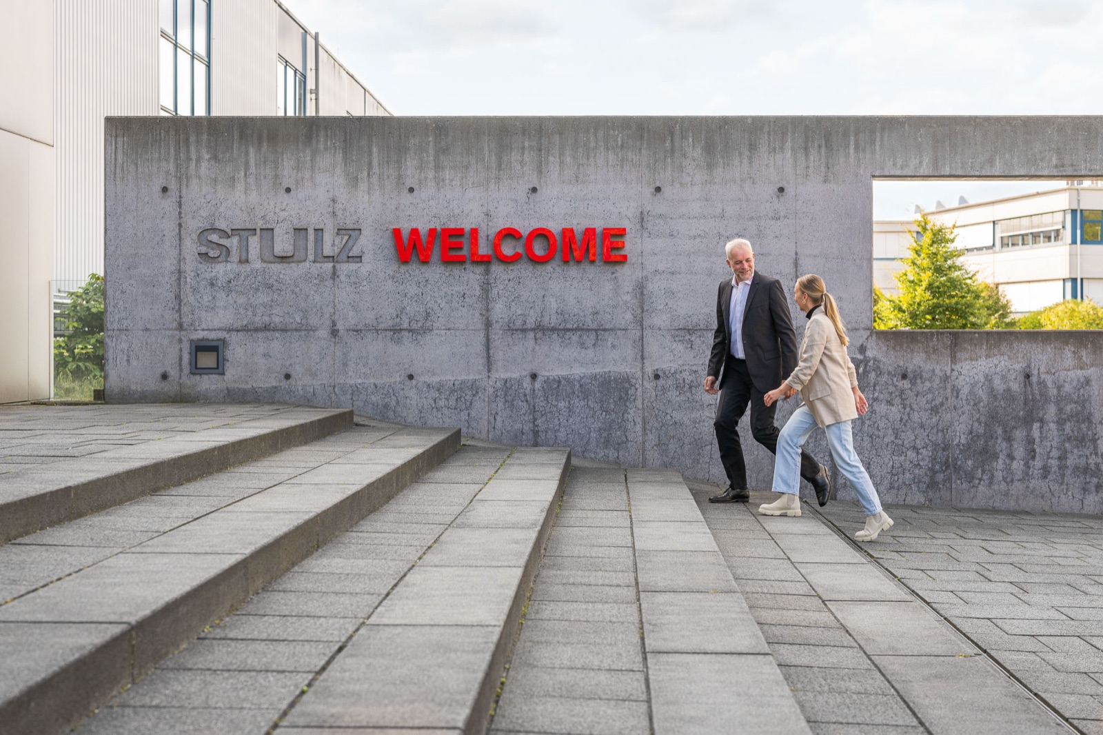 Zwei Personen vor der Betonwand mit dem Schriftzug STULZ WELCOME am Eingang