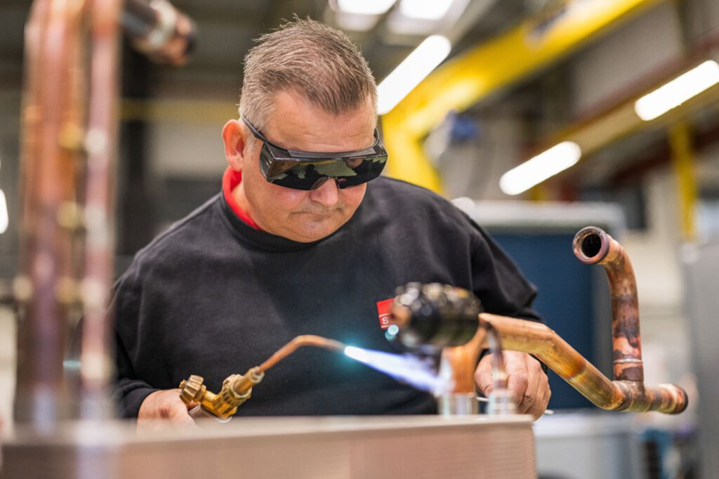 Mitarbeiter mit Schutzbrille lötet eine Kupferleitung in der Rohrvorfertigung von STULZ
