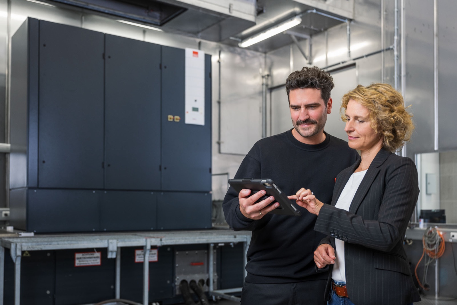 Zwei Personen mit Tablet vor einer großen Klimaanlage im Testcenter von STULZ