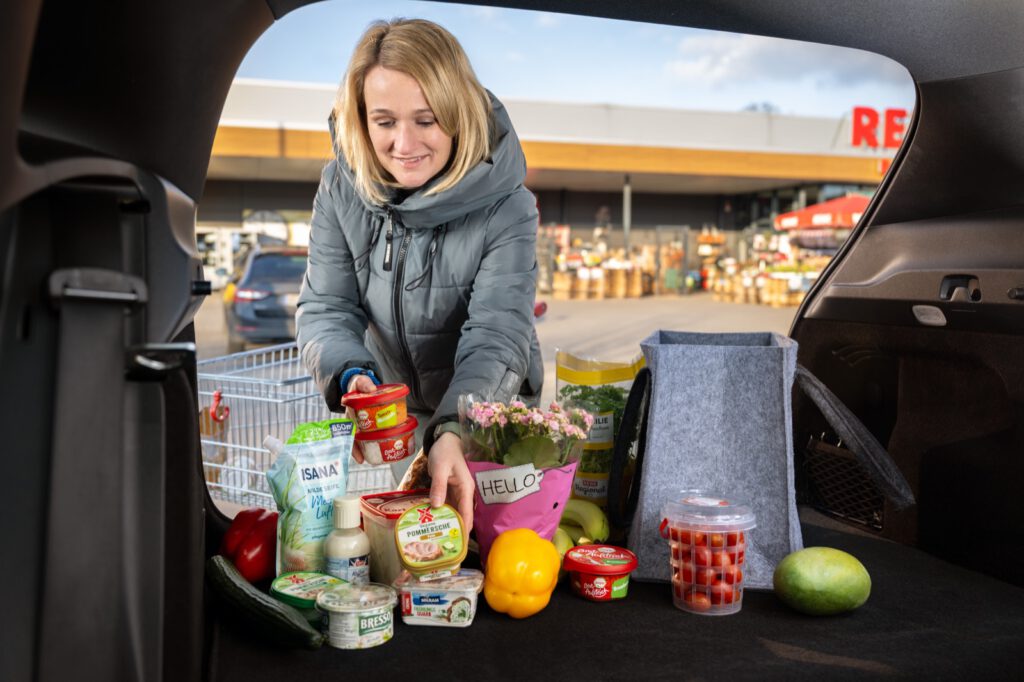 Frau lädt vor dem Supermarkt ihren Einkauf in den Kofferraum