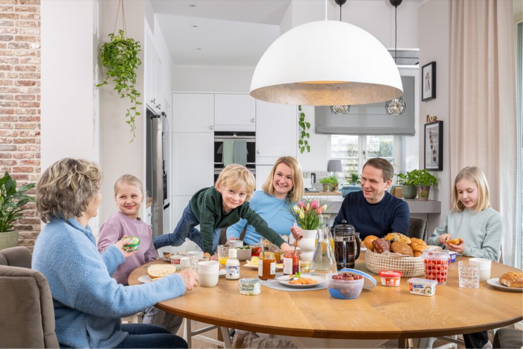 Familie am runden Frühstückstisch, auf dem Tisch Becher und Verpackungen