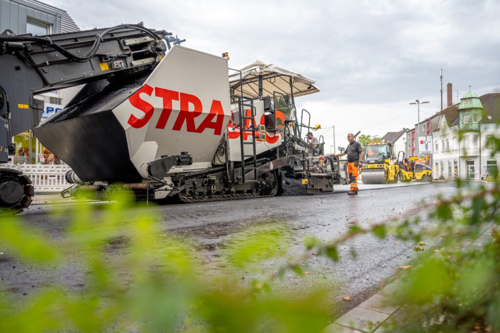 Einbauzug von STRABAG auf der Augustastraße in Dinslaken, im Vordergrund unscharfes Grün