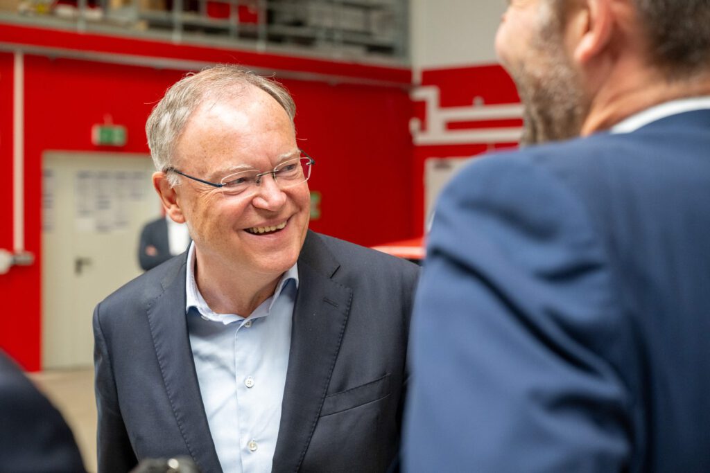 Stephan Weil lacht im Gespräch in der Fahrzeughalle von Alpha Robotics