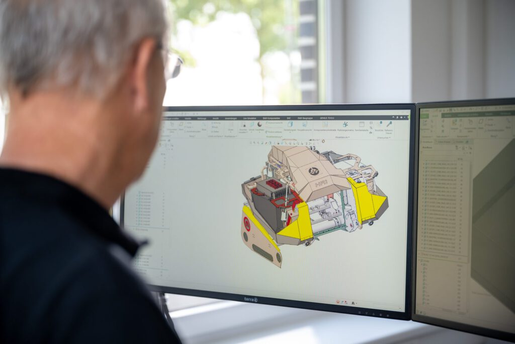 Ein Mitarbeiter von Alpha Robotics vor einem Monitor mit dem CAD-Modell des Superwolfs