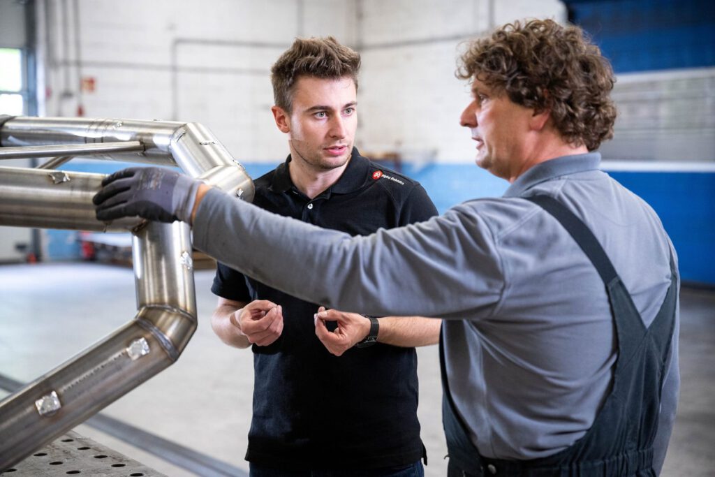 Ein Mitarbeiter von Alpha Robotics und ein Mitarbeiter der Schweißerei sprechen am Rohrrahmen