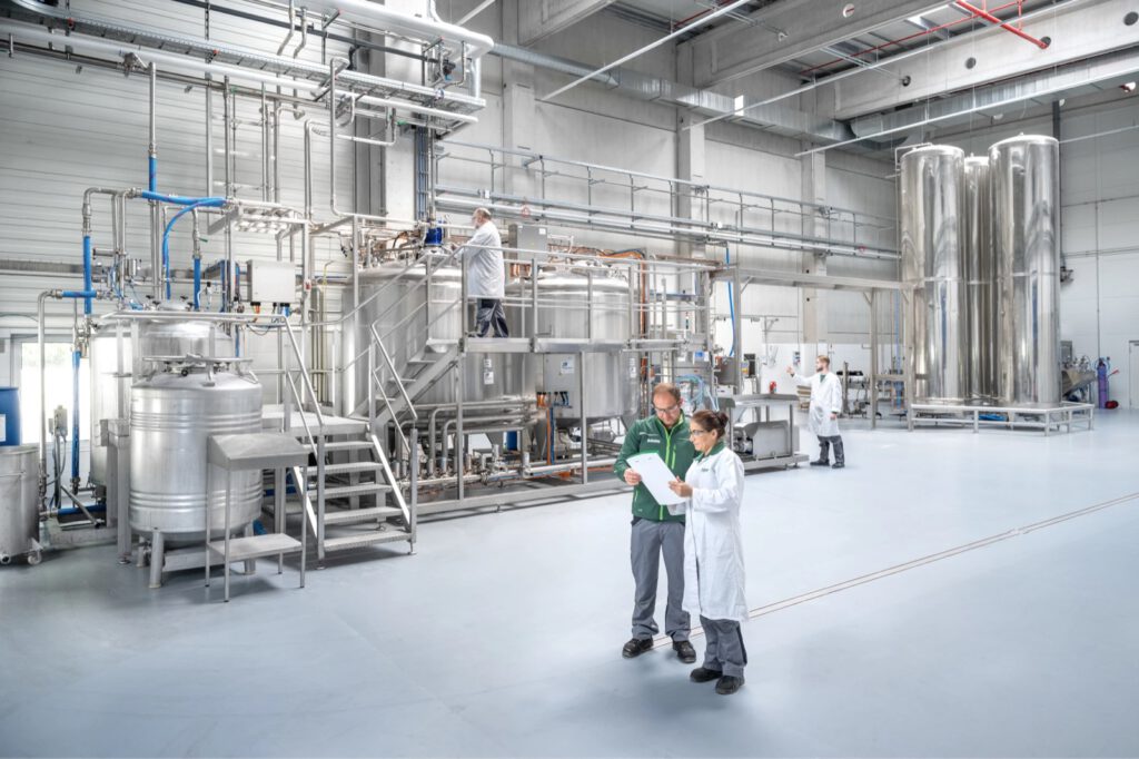 Ein Mitarbeiter in grüner Jacke und eine Kollegin im Laborkittel mit Unterlagen in der Flüssigproduktion von Biochem
