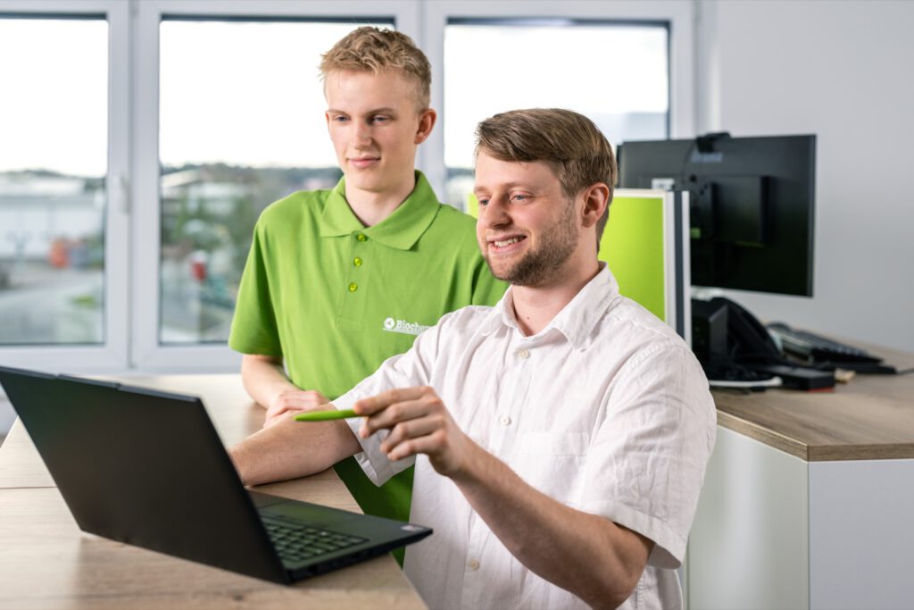 Ein Auszubildender und ein Kollege besprechen etwas am Laptop im Büro