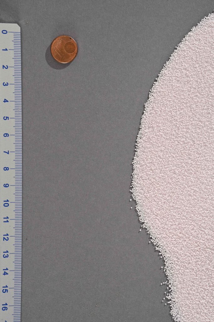 Hellrosa Pulver auf grauem Grund, daneben ein Lineal und eine Cent-Münze als Größenvergleich